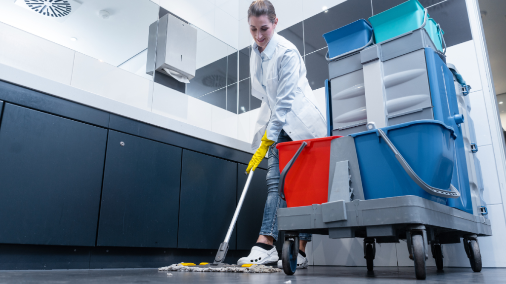 Commercial janitorial worker mopping a restroom floor with cleaning cart nearby